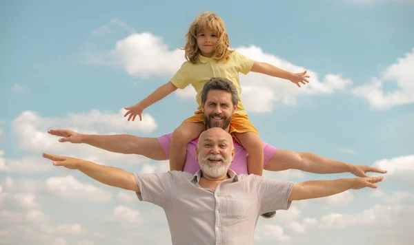 Ojciec, syn i dziadek szczęśliwa rodzina wielogatunkowa z podniesionymi rękami lub otwartymi ramionami latającymi na niebie. Ludzie pokoleń. — Zdjęcie stockowe