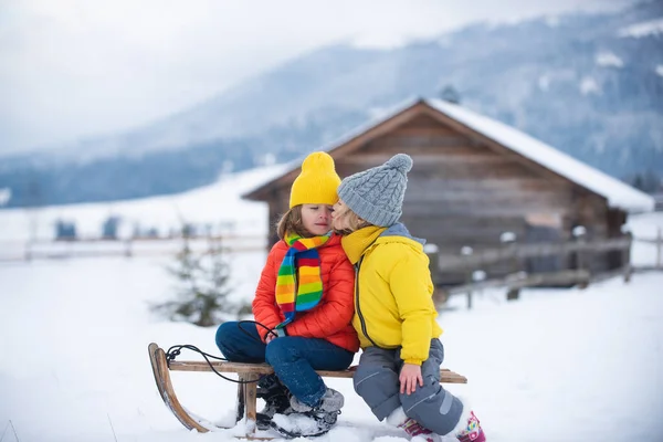 Children kissing. Happy little children and sledding in winter. Kids kiss on snow slides in winter. Son and daughter enjoy a sleigh ride. — Stock Photo, Image