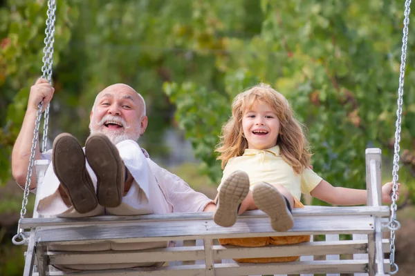 Excited amazed grandson child and grandfather swinging in summer garden. Granddad and grandchild having fun on a swing together in summer garden outdoors. Weekend with granddad. — Stock Photo, Image