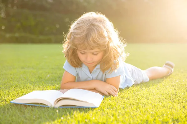 Okos gyerekek. A kisfiú könyvet olvas a nyári napnyugtakor. Nyári szabadtéri gyerekek oktatás. — Stock Fotó