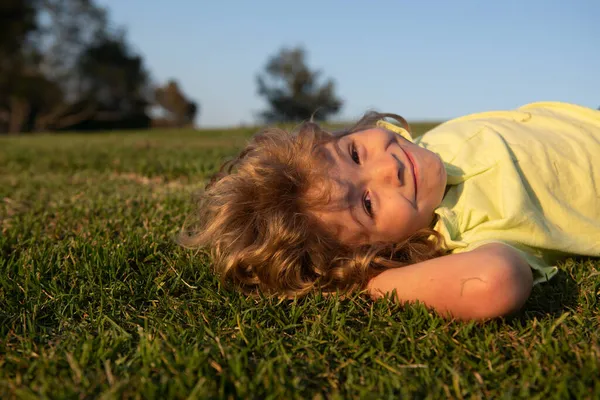 Söt, glad pojke som leker på ett gräs i en park vid en källa. Skrattar, njuter av färskt. Roliga barn. — Stockfoto