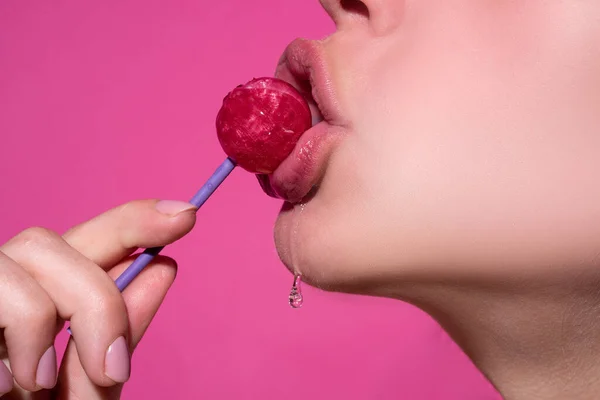 Orgazmus koncepció. Nyalóka a szájban, közelkép. Gyönyörű lány száj nyalókával. Fényes, vörös ajkak nyelvvel. Szájnyalás szívás chupa chups elszigetelt rózsaszín. — Stock Fotó