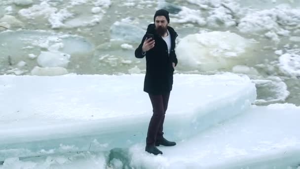 Hombre de invierno haciendo selfie al aire libre en un río congelado. Peligroso hielo delgado. Agua con hielo roto en el río, trozos de hielo. Superficie de hielo roto de un río en temporada de invierno helada. — Vídeo de stock