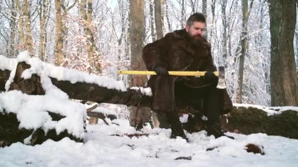 Egy jóképű férfi favágó szakállal télen. Favágó munkás sétál a hóerdőben fejszével. — Stock videók