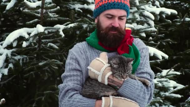 Zimowy mężczyzna na zewnątrz w lesie śnieżnym. młody przystojny mężczyzna w zimowym ogrodzie przytula a kot. — Wideo stockowe