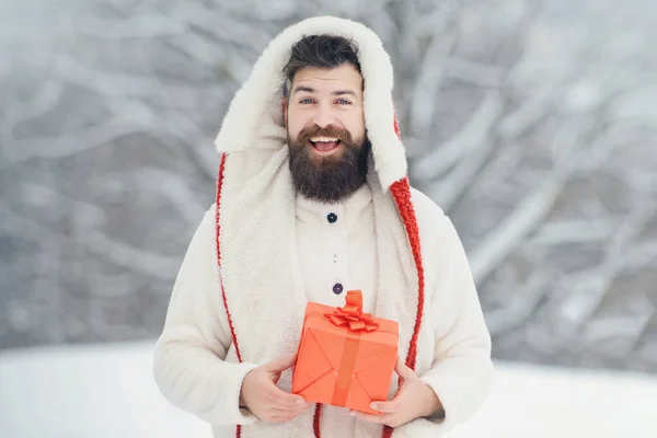 在雪地里,英俊的嬉皮士带着礼物的圣诞画像使雪人成为雪人.红色礼物的男人。留着胡子的英俊男人，留着胡子的圣诞老人 — 图库照片