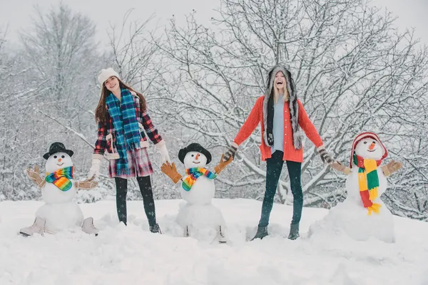 Grupo de chicas con muñeco de nieve al aire libre. Estudiantes fiesta de invierno y celebración de Navidad. Dos jóvenes alegres divirtiéndose con muñeco de nieve. Feliz Navidad y Feliz Año Nuevo. — Foto de Stock