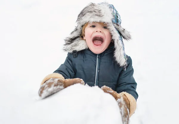 Aufgeregtes Kind, das mit einem Schnee spielt. Nettes Kind mit Wintermütze, das Spaß mit Schneeball im Winterpark hat. Winterbekleidung für Kinder. — Stockfoto