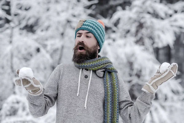 Homem barbudo com bolas de neve na floresta nevada. Cuidados com a pele, cuidados com a barba no inverno. Hipster em casaco, chapéu, cachecol, barba quente no inverno. Luta de neve, descanso de inverno — Fotografia de Stock