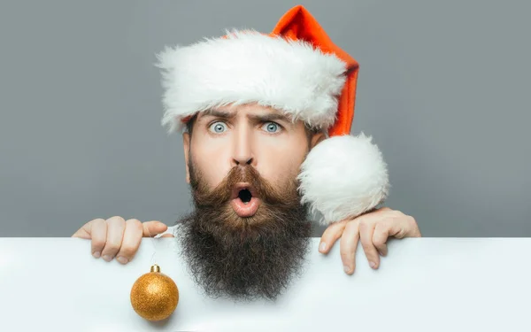 Hombre barbudo con barba larga y bigote en la cara sorprendida con cartulina sobre fondo gris. Hombre en Navidad —  Fotos de Stock