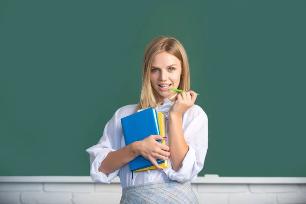黒板を背景に教室で勉強する若い女子大生の肖像画。創造的な若いです笑顔女性学生とともにペンと本. — ストック写真