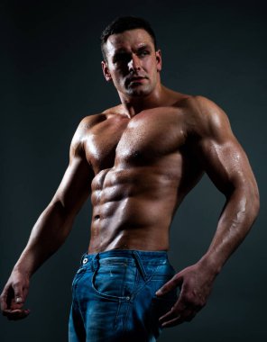 Sexy caucasian man in jeans standing with naked torso, guy showing six-pack abdominal abs, have perfect body, dark black background. clipart