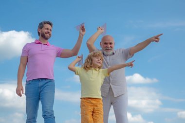 Büyükbaba ve oğul gökyüzünde kağıt uçakla oynuyorlar. Mutlu bir aile. Üç erkek nesli. Mutlu çocukluk.
