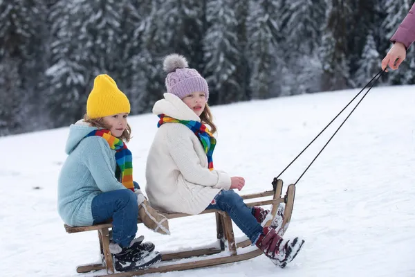 坐雪橇的孩子们。孩子们，男孩和女孩在外面的雪中玩耍。冬天、假日和圣诞节。家庭圣诞假期户外. — 图库照片