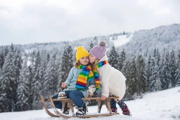 Дети на санях. Мальчик и девочка играют на улице в снегу. Зимние каникулы. Рождественский пейзаж. — стоковое фото