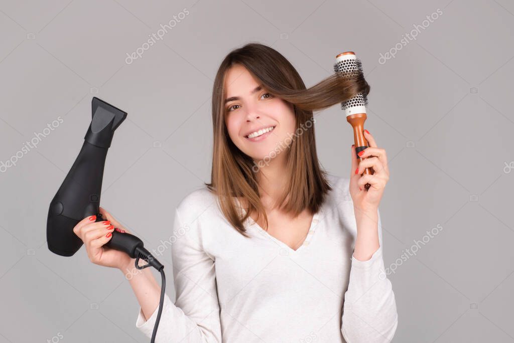 Young woman with hair dryer. Beautiful girl with straight hair drying hair with professional hairdryer.