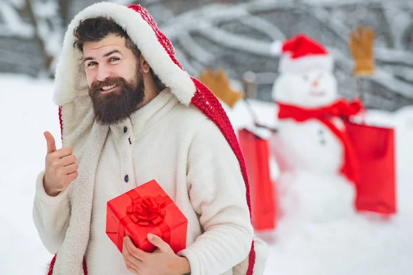 Uomo d'inverno. Pupazzo di neve e divertente uomo barbuto con dono. Buon padre con regalo di Natale su sfondo pupazzo di neve inverno. — Foto Stock