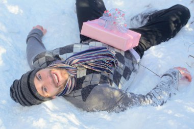 Mutlu kış adamı hediyesiyle karda yatıyor.