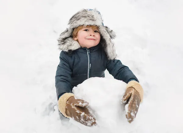 Nettes Kind mit Wintermütze, das Spaß mit Schneeball im Winterpark hat. Winterbekleidung für Kinder. — Stockfoto