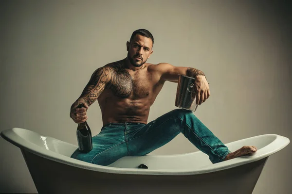 Homme musclé assis sur la baignoire dans la salle de bain, les hommes vacances avec du champagne. Célébrer Noël ou anniversaire. Partie de sexe privé. — Photo