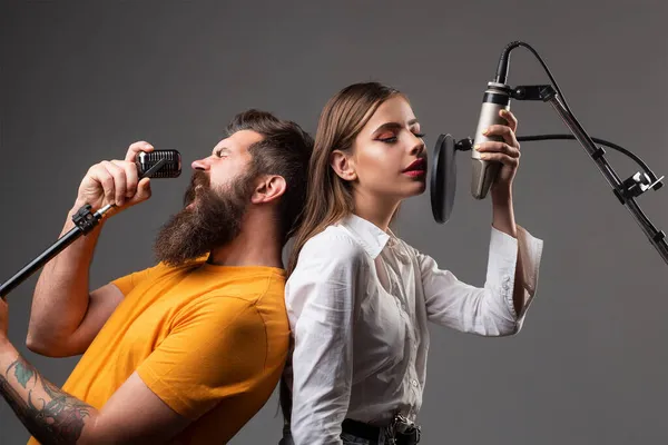 Uomo e donna con volti eccitati godono della musica. Coppia di cantanti sta eseguendo una canzone con un microfono durante la registrazione in uno studio musicale. — Foto Stock