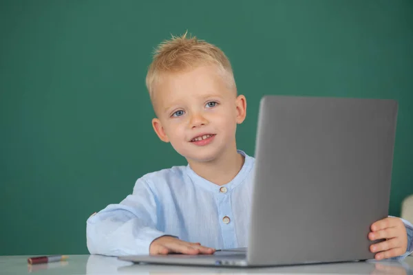 Een jongetje met een laptop op school. Leuke pupil gezicht close-up op schoolbord achtergrond. — Stockfoto