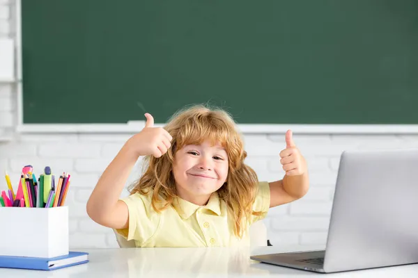 Opgewonden kind jongen gezicht met duimen tot het leren van les op school, het maken van huiswerk en met behulp van notebook gadget. — Stockfoto