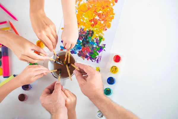 Lidská ruka otce a dětí kreslí barevnými tužkami. Horní pohled na bílý stůl s uměleckými potřebami. — Stock fotografie