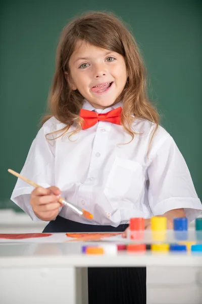 Sanat ve zanaat derslerinin tadını çıkarırken mutlu bir şekilde gülümseyen komik dilli kızın portresi. Okuldaki çocuk boyalarla resim çiziyor. Çocukların yaratıcılığı. Komik çocuk duyguları.. — Stok fotoğraf