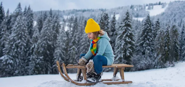 Portrét šťastného malého kluka v pleteném klobouku, šále a svetru. Chlapec si užívá jízdu na saních na zimní krajině. Dítě sáně na saních venku ve sněhu. Zimní pletené dětské oblečení. — Stock fotografie