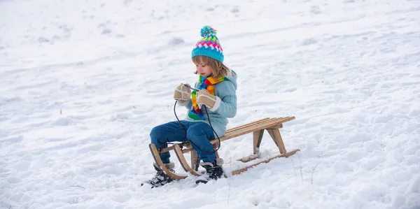 子供のためのアクティブな冬の屋外ゲーム。クリスマス休暇のコンセプト。冬を楽しむ少年は、冬の森の中でそりに乗って遊んでいます。雪の背景コピースペース,バナー. — ストック写真