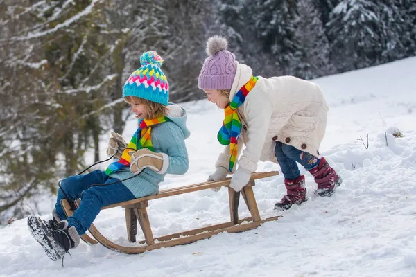 Rolig pojke och flicka som har kul med en släde på vintern. Söta barn som leker i snö. Vinteraktiviteter för barn. Kalla och snöiga vinterberg. — Stockfoto