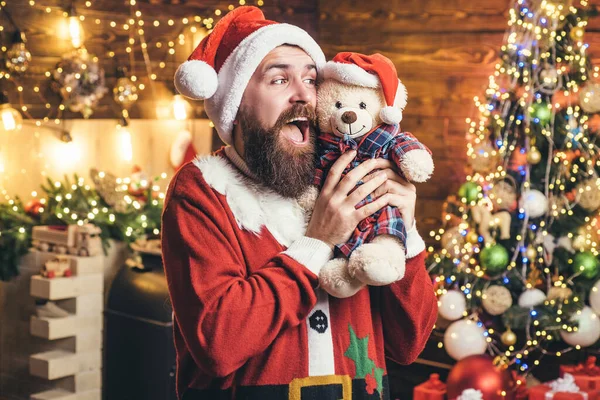 Der Weihnachtsmann wünscht Weihnachten. Der bärtige moderne Weihnachtsmann im Strickpullover mit Spielzeug-Teddybär. — Stockfoto