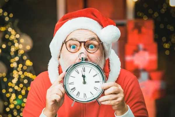 Aufgeregt hält der Weihnachtsmann die Uhr an. Foto vom Weihnachtsmann, der auf die Uhr zeigt, die fünf Minuten vor Mitternacht zeigt. — Stockfoto