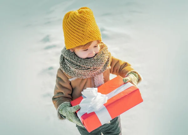 Malý chlapec v teplých zimních šatech drží dárkovou krabici. Světlé oblečení pro děti. — Stock fotografie