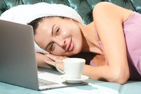 Bella giovane donna sensuale con caffè e laptop in pigiama godendo il tempo libero mattutino in camera da letto a casa. — Foto Stock