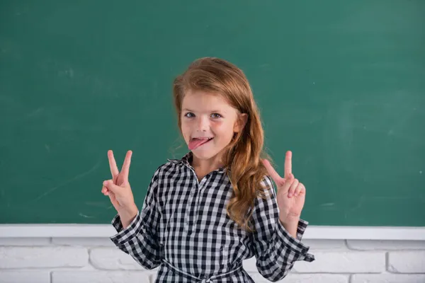 Retrato de aluna engraçada do estudo da escola primária. Miúda engraçada na escola. Criança do ensino fundamental em sala de aula. Lingua divertida. De volta à escola. — Fotografia de Stock