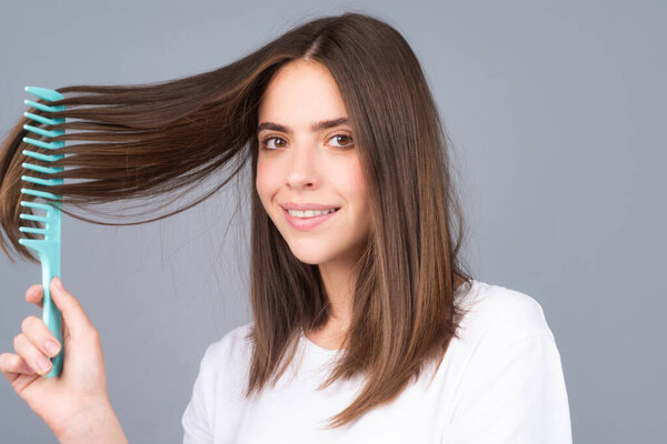 Smiling woman brushing hair with comb. Beautiful girl combing long hair with hairbrush.