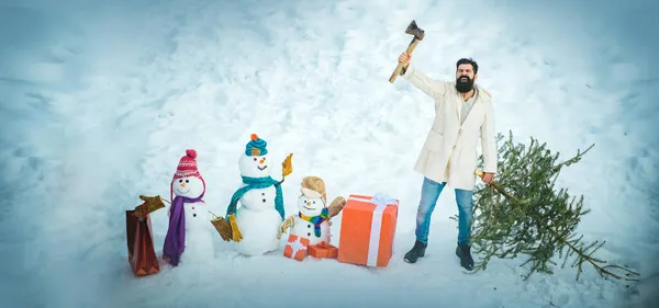 Glücklicher Vater mit Weihnachtsbaum und Schneemann auf einem verschneiten Winterspaziergang. Holzfäller mit Axt im Winterwald. — Stockfoto