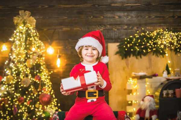 Портрет смешного парня с подарком, смотрящего в камеру. Ребенок веселится возле елки в помещении. — стоковое фото