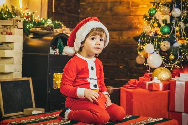 Симпатичный мальчик Санта с новогодними подарками на рождественском фоне. Эльфийское дитя. Подарки для зимнего отдыха у камина. — стоковое фото