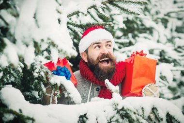 Heyecanlı adam hediye kutusunu dışarıda tutuyor. Kış karlı ormanda Noel Baba şapkalı sakallı adam.