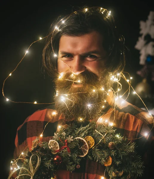 Vánoční muž s vousy na šťastném obličeji a věnci. Garland na Santa Claus muž jako dekorace držet věnec — Stock fotografie