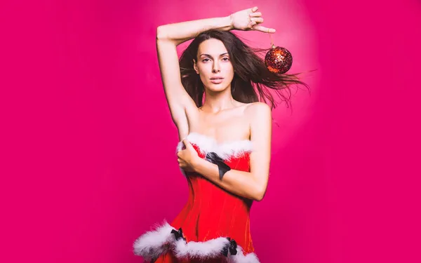 Kırmızı Noel Baba elbiseli seksi kadın kırmızı arka planda stüdyoda dekoratif balo düzenliyor. — Stok fotoğraf
