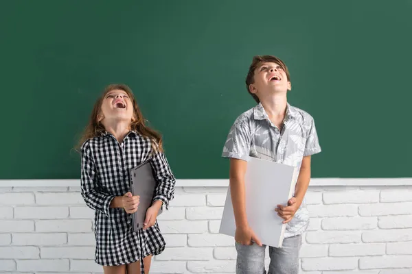 Los niños de la escuela tienen un libro con una expresión sorprendente contra la pizarra. Escuela niños amigos. —  Fotos de Stock