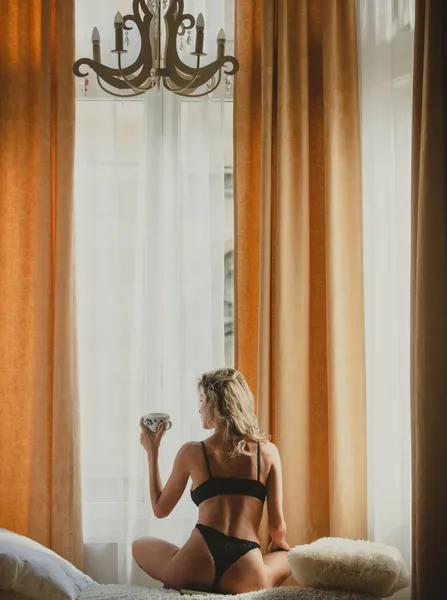 Вид ззаду на молодих здорових жінок у спальні. Вранці п'є каву. Розслаблена молода чуттєва жіноча модель з чашками кави в ліжку вдома. Весела сексуальна ранкова дівчина . — стокове фото
