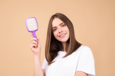 Kadın tarak ile saç stili yapıyor. Stüdyoda sağlıklı ve parlak saçları olan güzel bir genç kadın. Saçını tarayan genç kadına yaklaş..