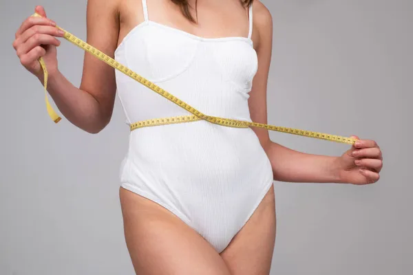 Concepto de alimentación saludable y dieta. Chica joven con cintura perfecta con una cinta métrica. Cuidado corporal. — Foto de Stock