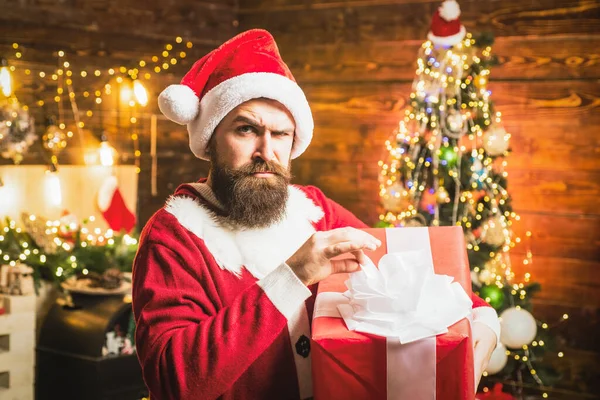 Hipster en Santa Sombrero rojo sosteniendo presente. Estilo Santa hombre con una larga barba posando sobre el fondo de madera de Navidad. —  Fotos de Stock