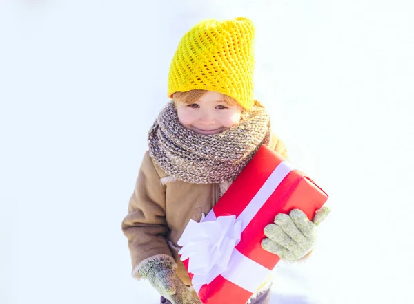 冬の子供の贈り物弓雪の背景を保持します。冬服の帽子とスカーフでかわいい男の子が閉じます。明けましておめでとうございます。. — ストック写真